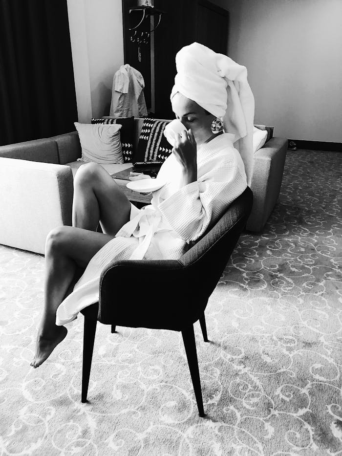 Chic woman in a bathrobe and towel turban, enjoying a drink indoors.